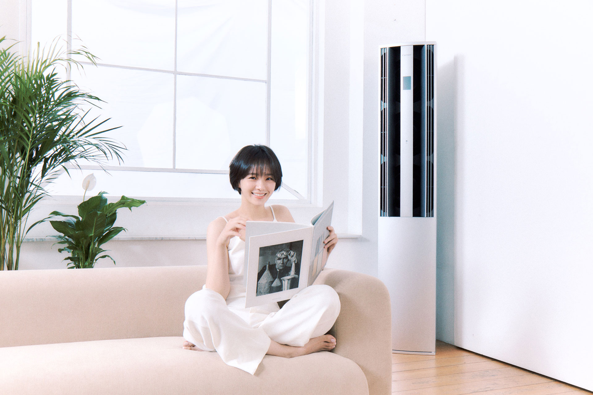 캐리어 앰베서더 박규영이 실내공기를 쾌적하게 순환시켜주는 캐리어가 있는공간에서 쇼파에 앉아 책을 읽으며 화사하게 웃고있다.